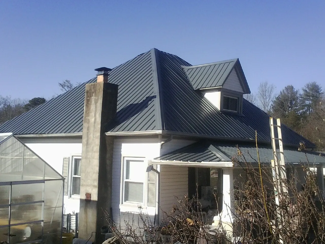 Dark blue standing seam metal roof on a white farmhouse with dormer — Slate & Tile Roof Repair by Roofing Brothers in Smith