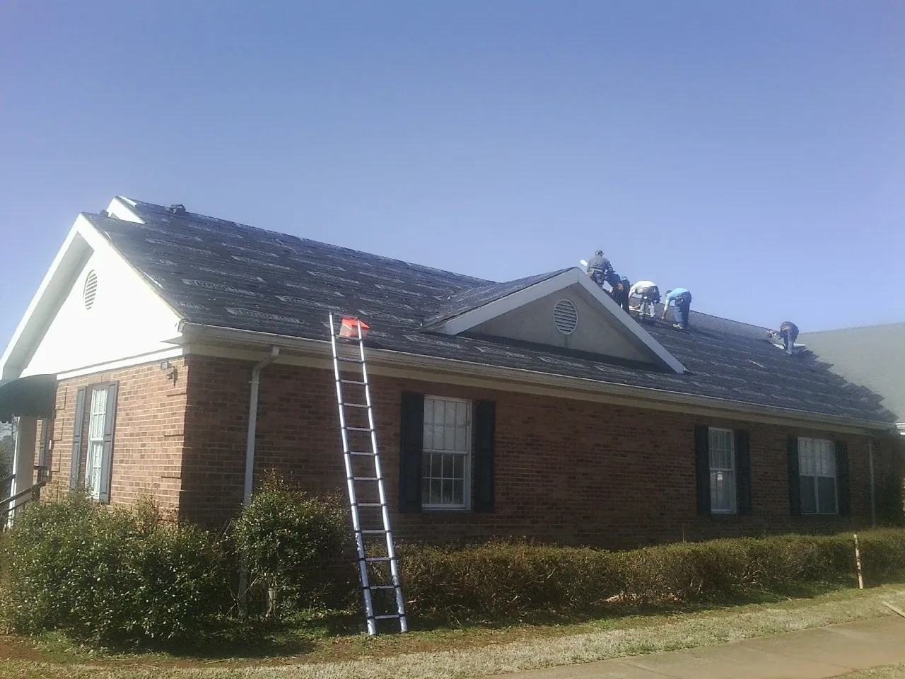 Crew tearing shingles off a brick ranch roof with a ladder set — Emergency Roof Repair work by our crew in Smith