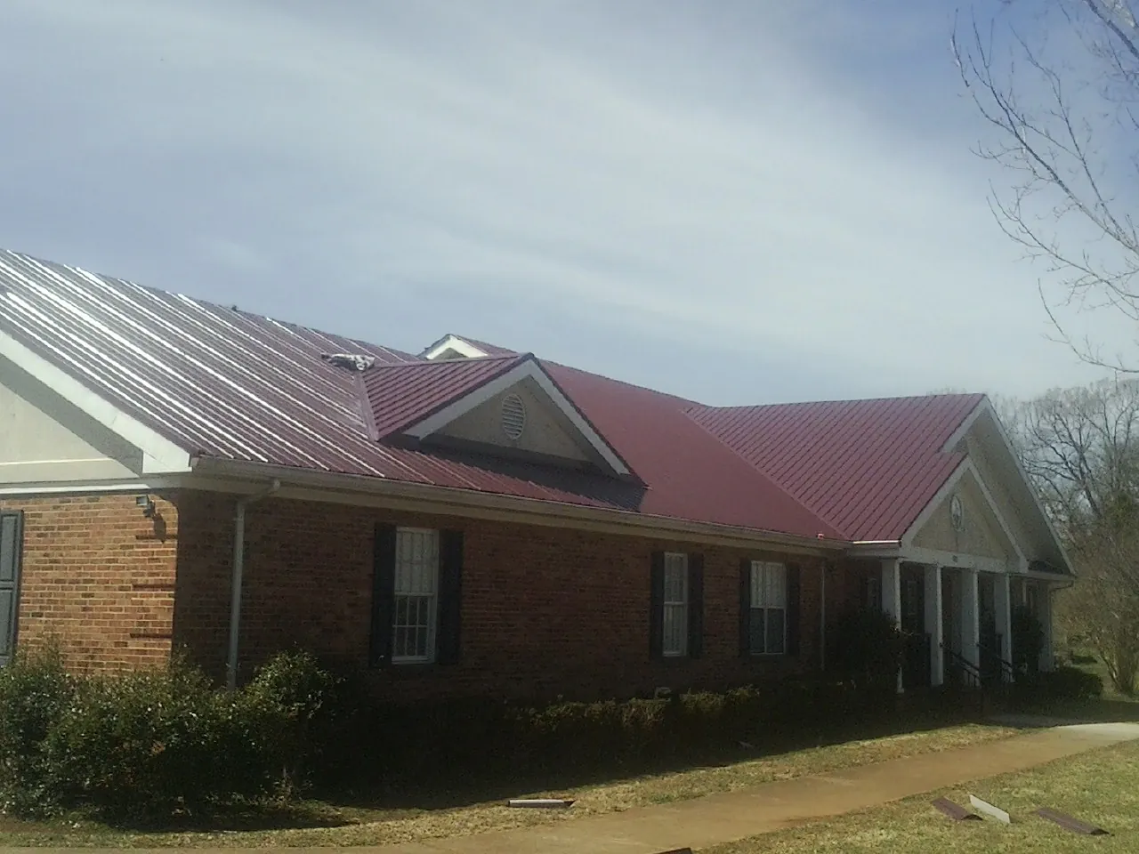 Red metal roof with gabled entries on a long brick building, from a Hail Damage Roof Repair job in Smith