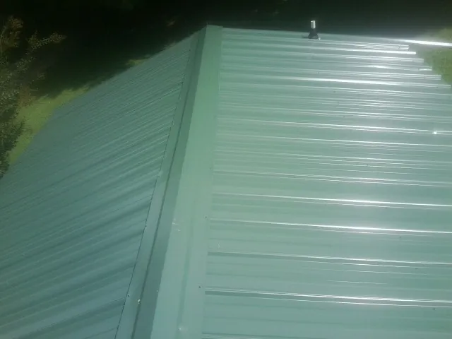 New green metal panels meeting at the ridge of a roof — Flat Roof Repair work by our crew in Smith