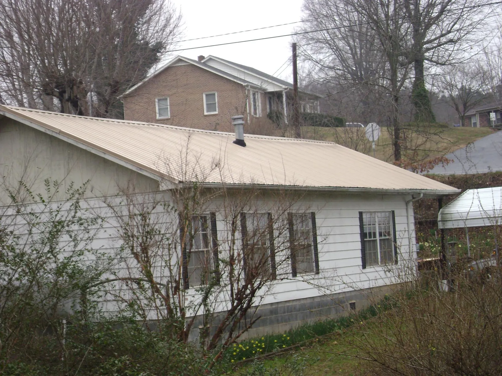Tan metal roof on a white sided house set into a hillside — Commercial Roofing by Roofing Brothers in Smith