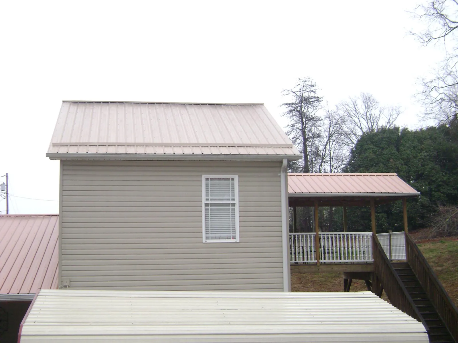 Tan metal roofs on a two story addition and attached porch, from a Roof Replacement job in Smith